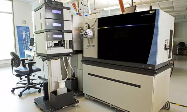Photograph of a laboratory instrument consisting of a large component on a mobile bench (the mass spectrometer), and a smaller component with stacked modules (the liquid chromatograph).