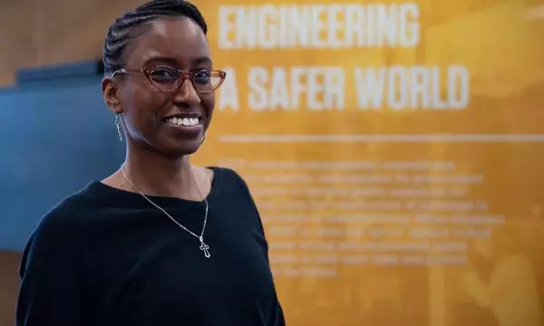 Jazalyn Dukes poses in front of a display that reads "Engineering a Safer World."