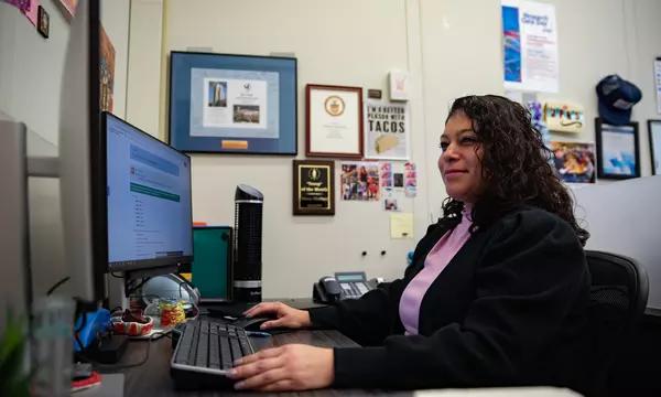 Serena Martinez sits at a computer workstation in an office setting. 