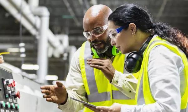 A man and woman work at a manufacturing dashboard.