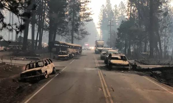 A two-lane highway lined with the burnt remains of vehicles that were destroyed by fire while in traffic.