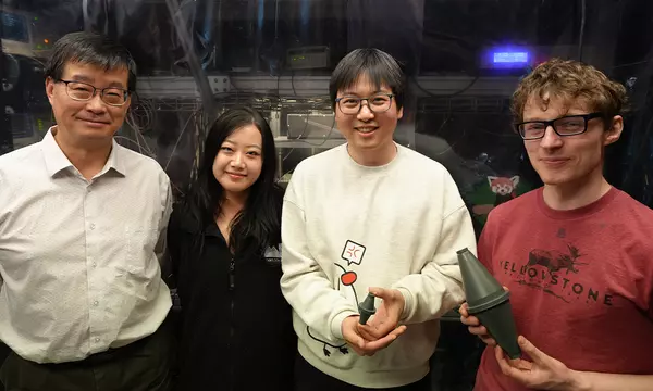 Four researchers, one older and three younger, pose in the lab holding models of a laser cavity.