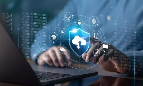Illustration shows cloud, cybersecurity and identity icons floating over an open laptop with a person's hands at the keyboard.