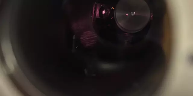 View through a circular opening into a dark interior. A red dot floats in the darkness. 