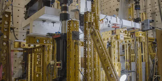 Horizontal concrete slab is visible in a forest of scaffolding and equipment in a large indoor space. 
