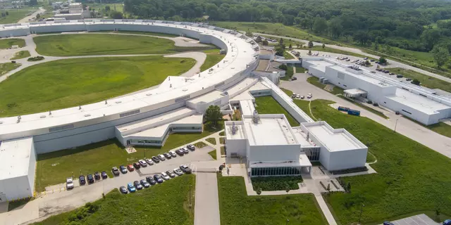 An arial view shows part of the huge enclosed loop of an accelerator, with attached buildings and parking lots.