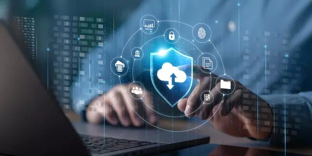 Illustration shows cloud, cybersecurity and identity icons floating over an open laptop with a person's hands at the keyboard.