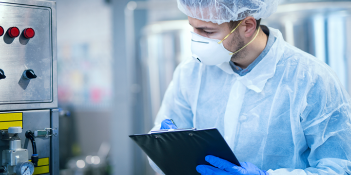 Technologist expert in protective uniform with hairnet and mask taking parameters from industrial machine in food production plant.