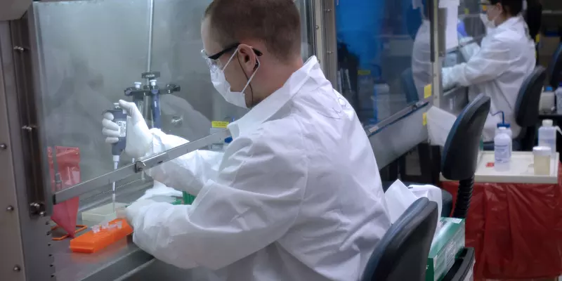 Man in white lab coat using a pipette under a hood