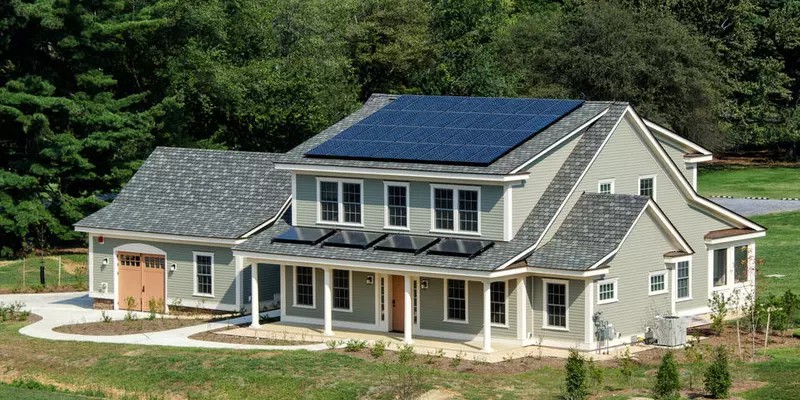 Photograph of large residential-style home with blue tile roof and solar panel in suburban campus setting.