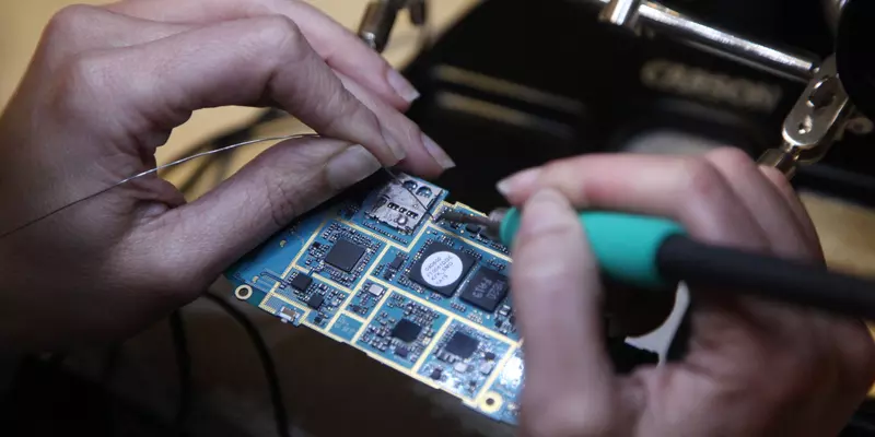 a person's hands as they use a soldering iron to attach wires to a circuit board.