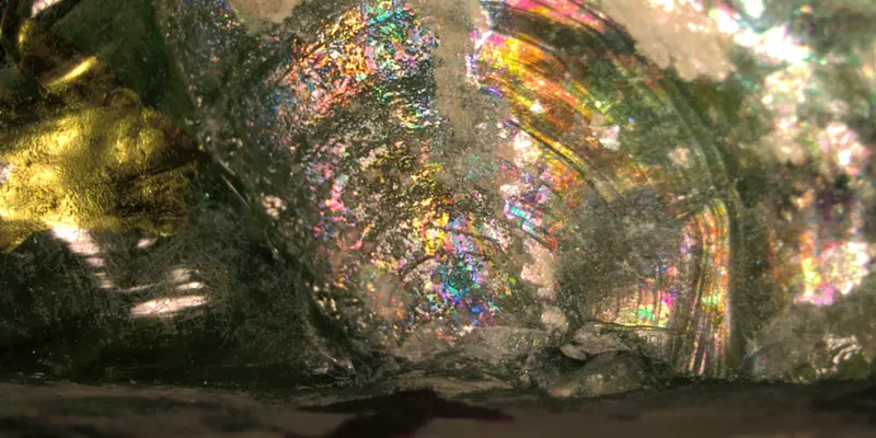 an opalescent close up of Roman glass. There is a clear semi-circular fracture in the center of the piece. 