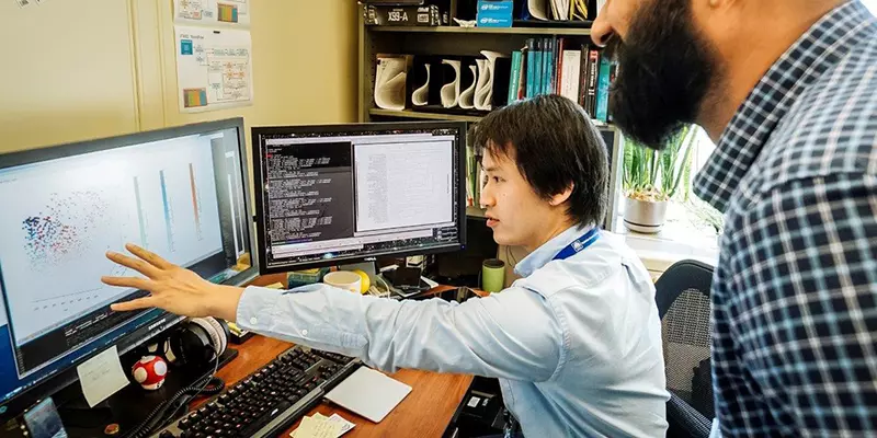 Tytus Mak sitting at his desk and while colleague Arun Moorthy and he look at a computer screen