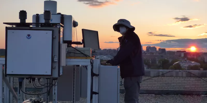 Man standing next to equipment on top of building during a sunset.  