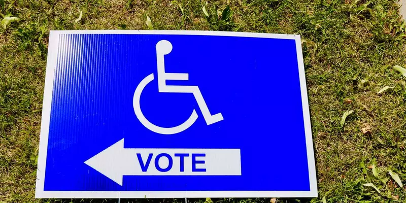 A polling station sign depicts an icon of a person in a wheelchair above the word "vote."