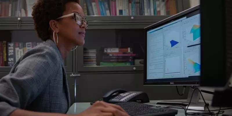 Side view of Danielle Brager at a desk, looking at a monitor, hand on a computer mouse.