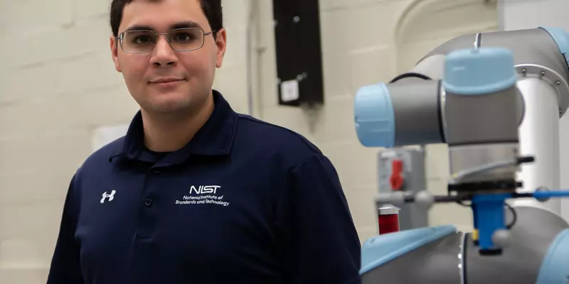 Omar Aboul-Enein poses next to a silver and blue robotic arm in a lab setting.