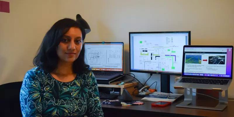 Nehika Mathur sits at a workstation with multiple computer monitors.