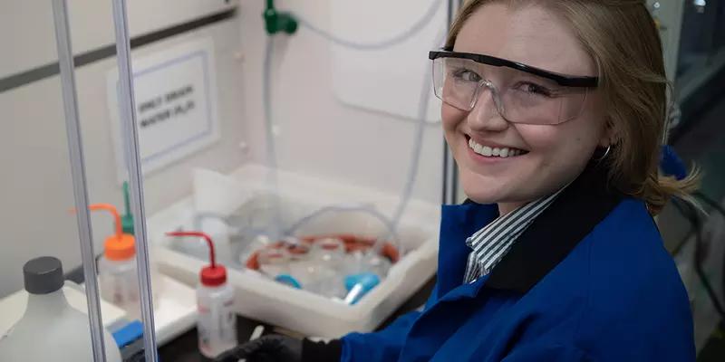 Christine McGinn wears safety glasses as she handles plastic bottles and other materials in the lab. 