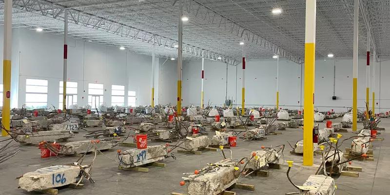 Concrete columns lay on their sides inside a warehouse with lots of space around each one.