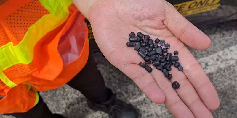 Someone wearing a safety vest holds up a handful of black plastic pellets.
