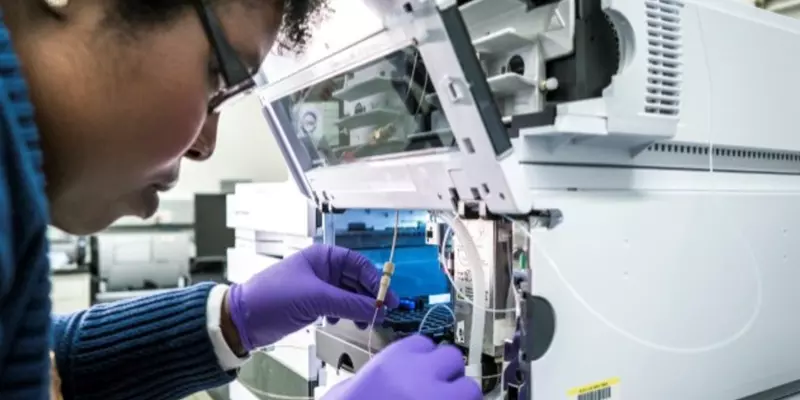 A researcher leans close to an open boxlike device, handling small tubes and vials inside.