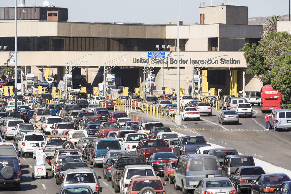 Dozens of cars waiting in a queue in front of a building with large letters reading, "U.S. Border Inspection Station."