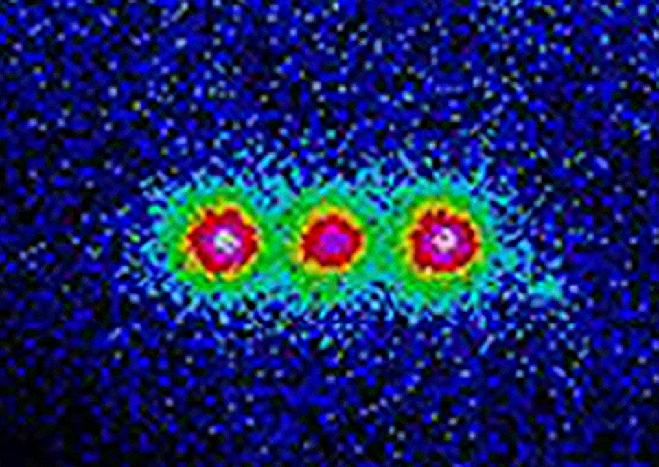 This colorized image shows the fluorescence from three trapped beryllium ions illuminated with an ultraviolet laser beam. 