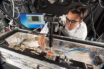 NIST's Zeehan Ahmed positions an optical fiber above a small photonic sensor inside an optical probe station