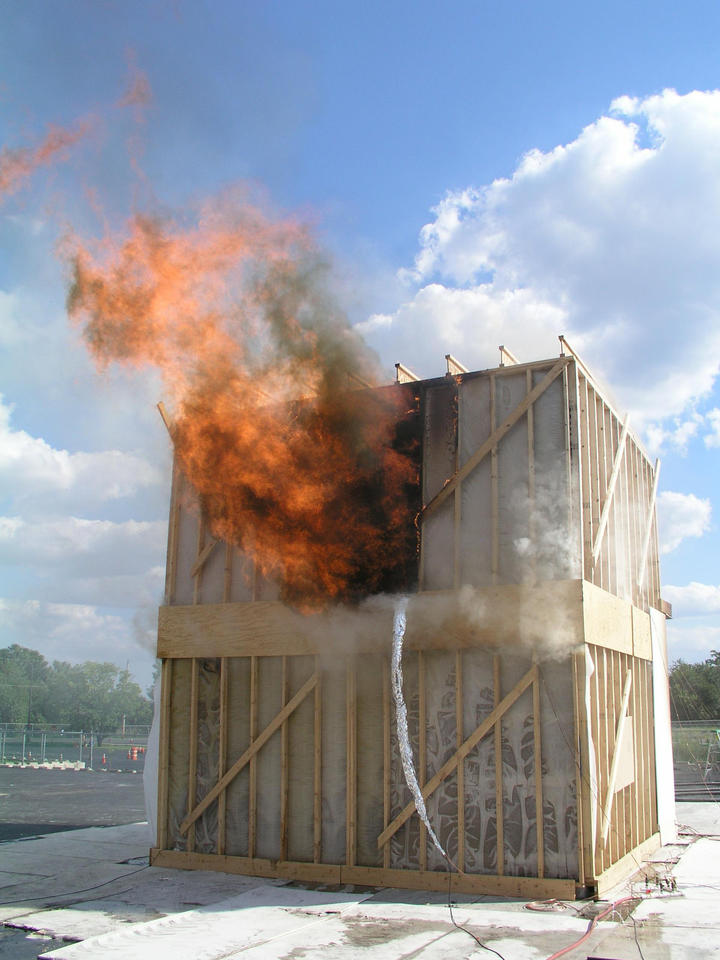 Flames coming out of the first doorway of a test structure after the floor has collapsed into the basement.