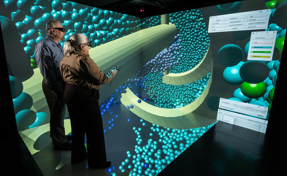 Photo of 2 researchers wearing visualization eyewear, standing in an immersive display which shows concrete particles.