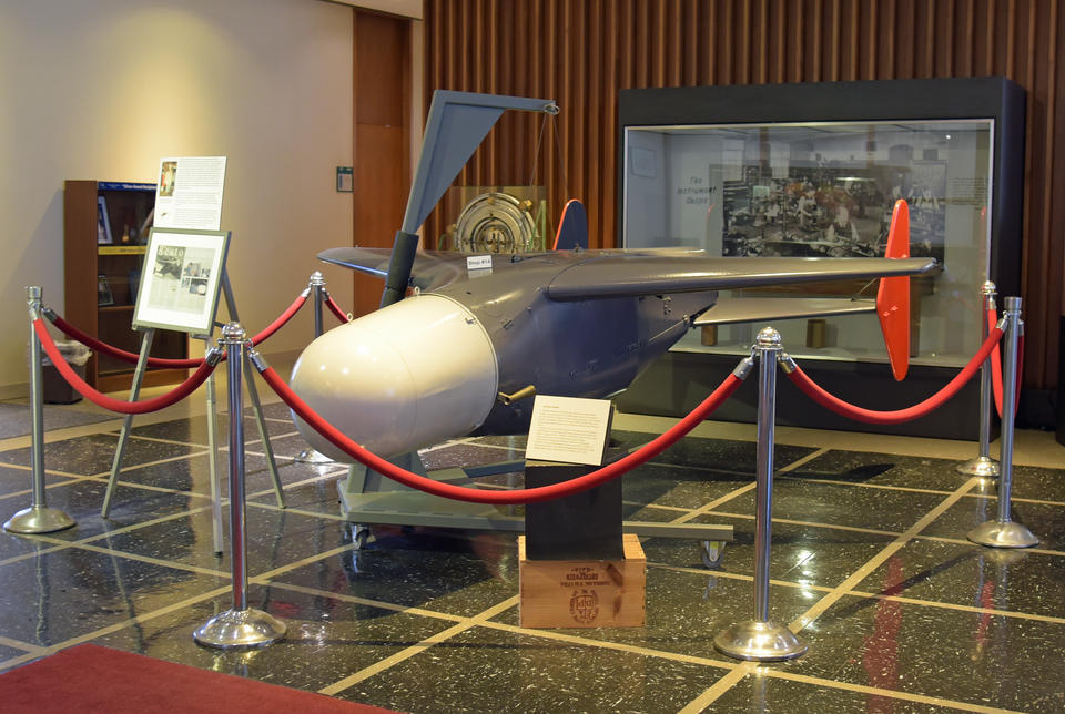 Photo of the restored Bat missile behind stanchions and ropes in the NIST library