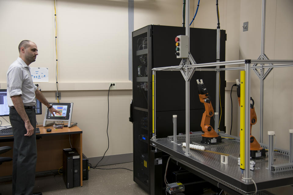 Timothy Zimmerman sending instructions to two small robotic manufacturing arms