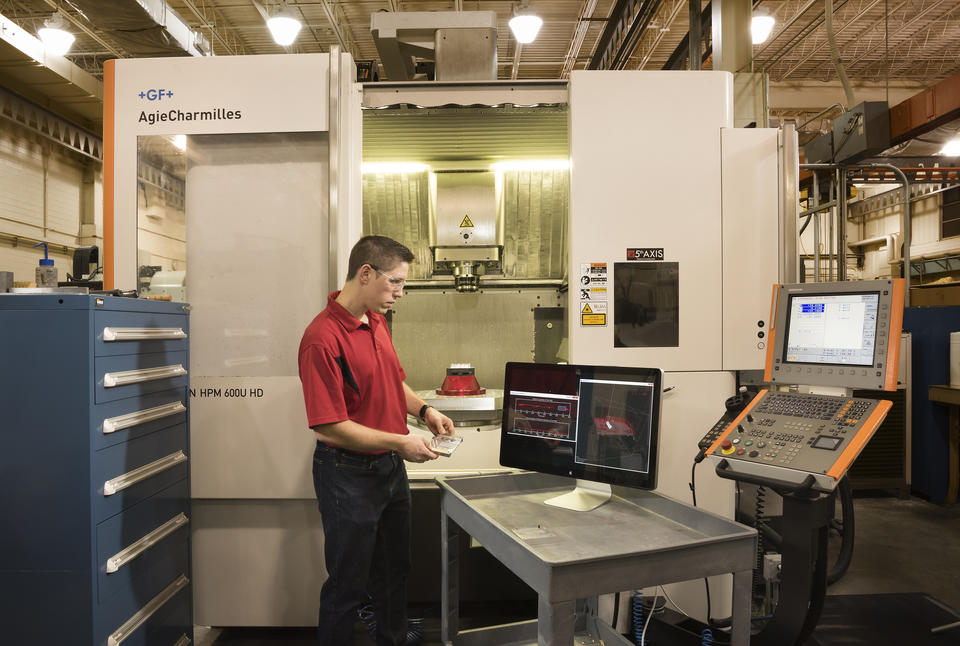 NIST researcher Tom Hedberg in a machine shop with computer monitor displaying CAD image