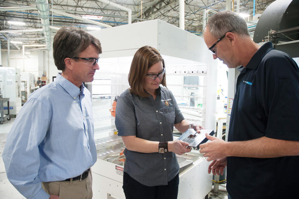 Three people on a manufacturing floor discussing a new product