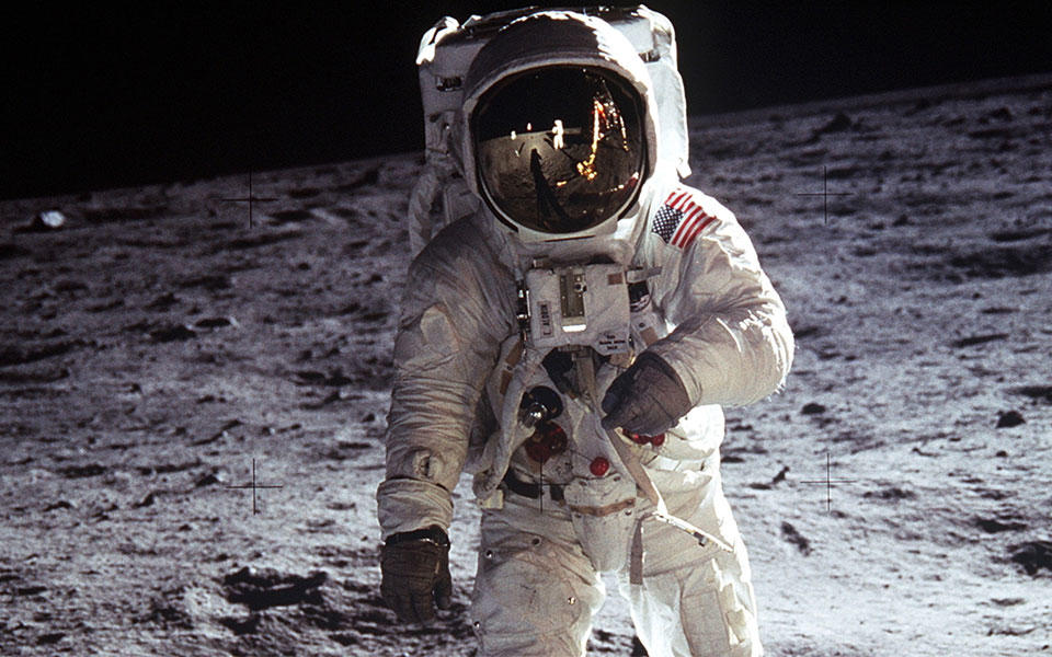 Photo of man in white space suite on surface of moon at night.