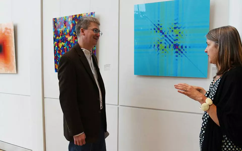Woman and man talking beside wall with several square illustrations of science art