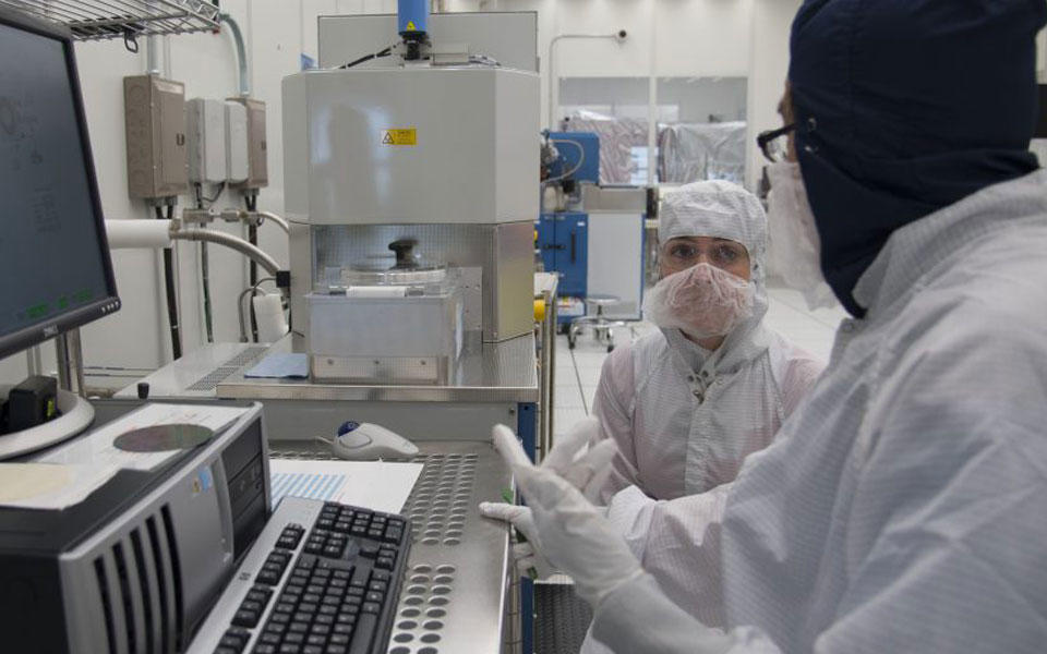Man and woman in lab gear in front of computer screen in clean room