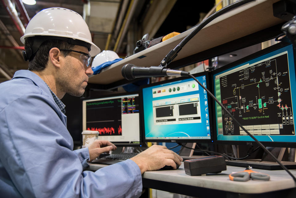 NIST Researcher in a hard hat watches three monitors that show data from a fire burn.