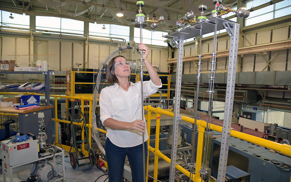 kate Ross holds a long pole used to put samples in front of a beam of neutrons  in the main hall at the NIST Center for Neutron Research. 