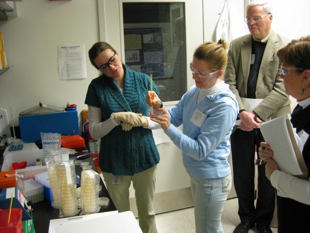 Two women work with a beaker while a man looks over their shoulder