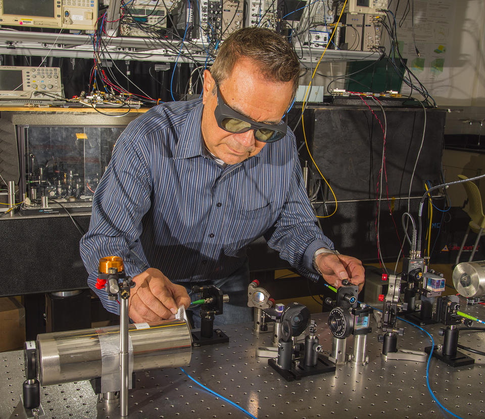 Man in striped shirt wearing laser safety glasses working with laser table in laboratory.