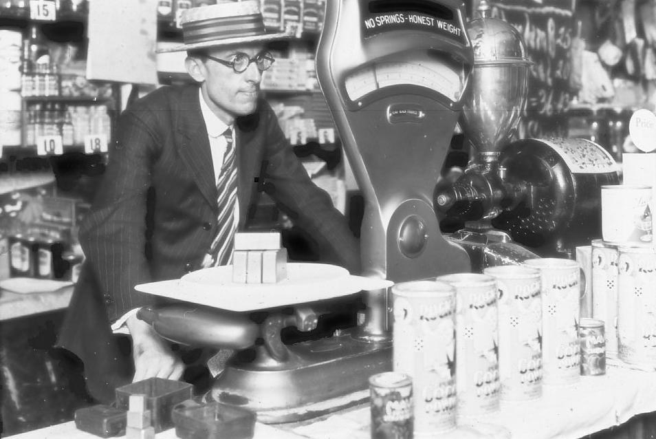 black and white photo of a 1920s weights and measures inspector checking the accuracy of a grocery store scale using test weights