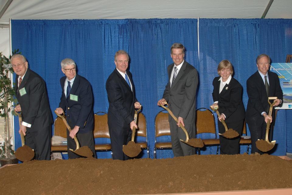 Six people with shovels stand in front of a pile of dirt