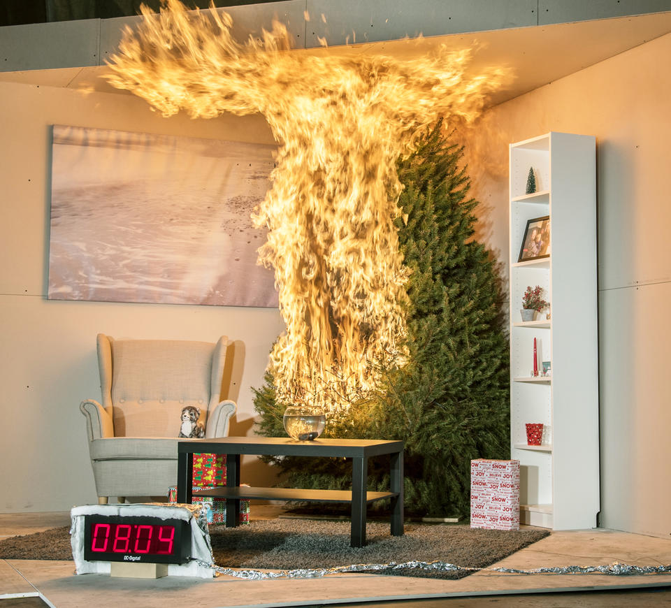 A Christmas tree is engulfed in flames. To the left is a chair. In front is a coffee table, rug and fishbowl. To the right is a tall bookshelf. There are 3 wrapped presents under the tree. A timer reads 8:04 seconds.