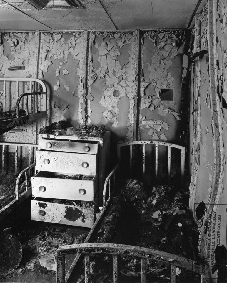 Black and white photo of post fire aluminum bedroom replica of SS united States ship in 1950. To the right and left there are burned bed frames and in the middle a burned dresser.