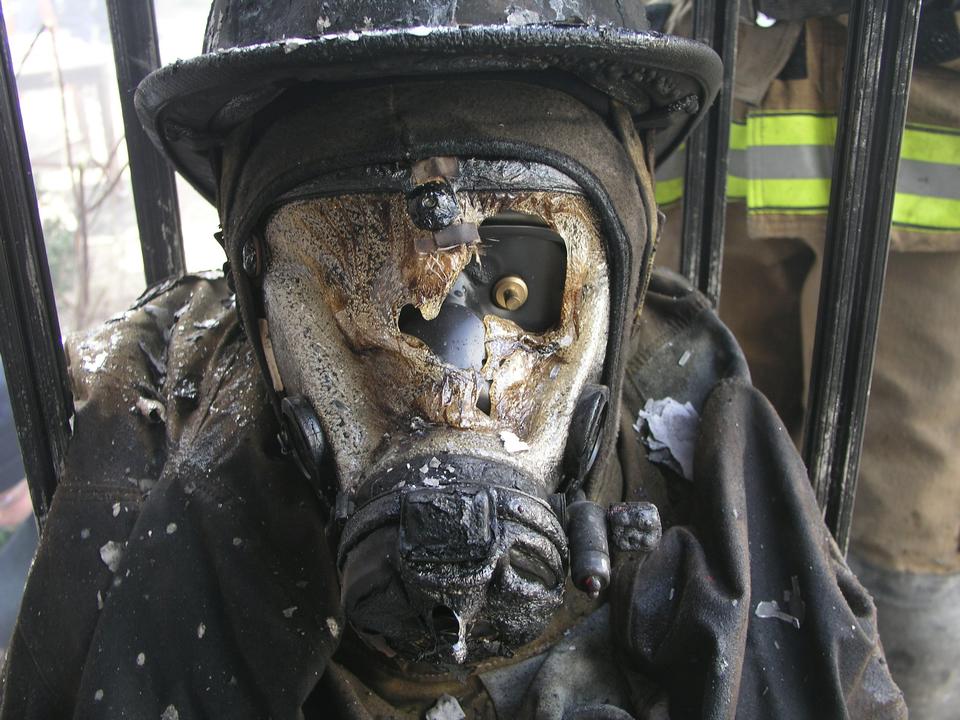 Closeup of firefighter face mask covered in char from fire burn. The rest of the uniform is also black, but in tact. 