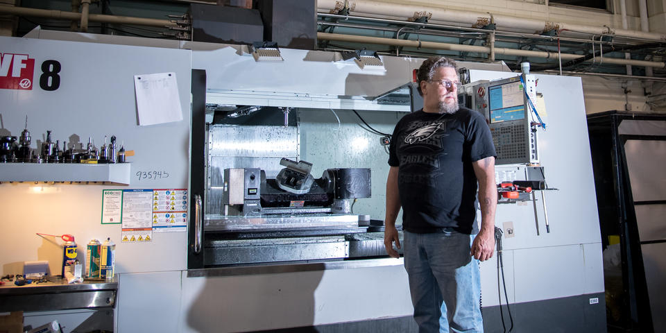 Luther Vulgamott stands in front of a five-axis computer numerical control machine