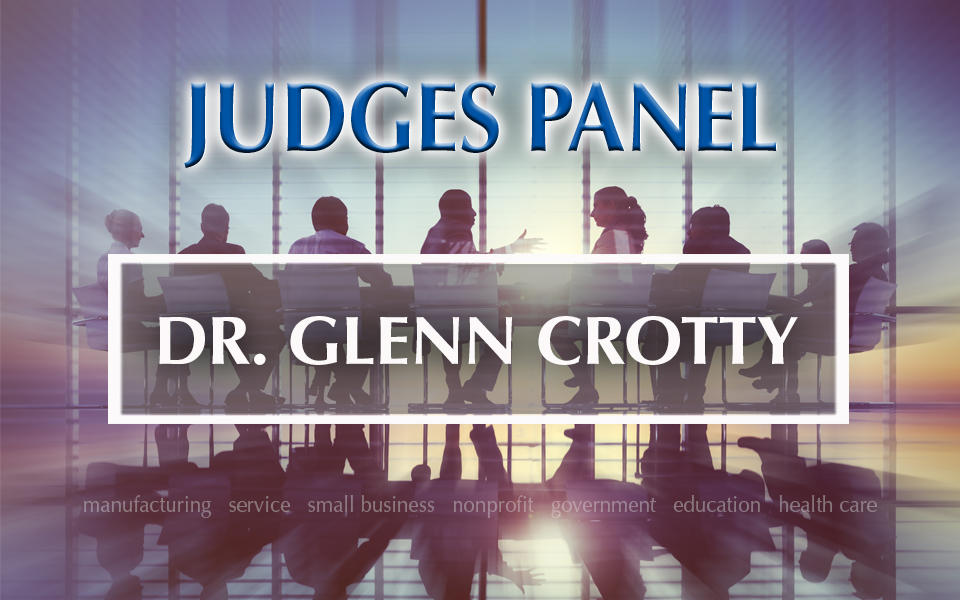 Judges Panel Dr. Glenn Crotty with photo in background of people meeting at a table.