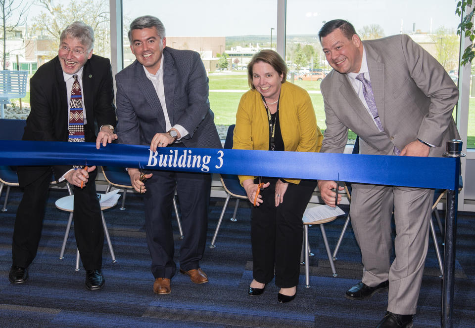 Four people with scissors get ready to cut a blue ribbon that says "Building 3" on it